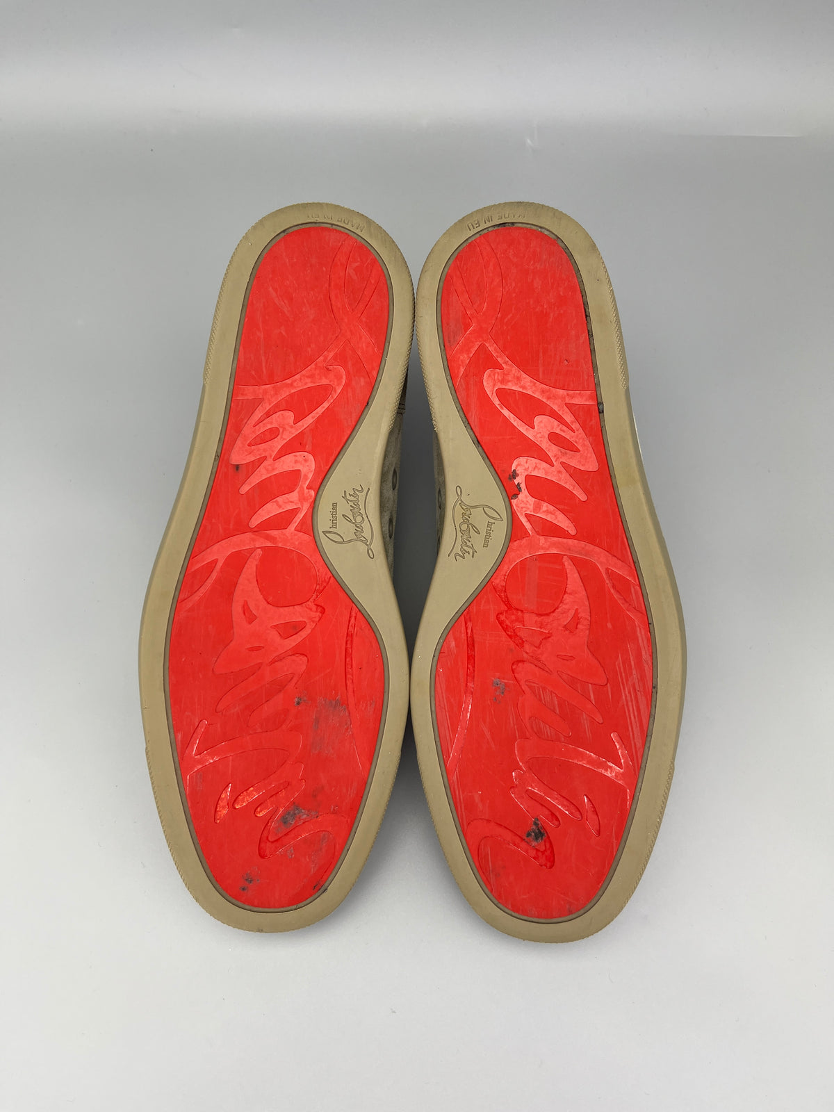 Red soles of shoes with a brand logo on a grey background